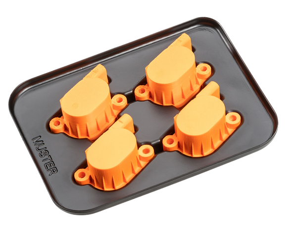 Vier orange 3D-gedruckte Bauteile auf einer schwarzen Anti-Rutsch-Matte. Jedes Bauteil hat einen geometrischen Körper und ist mit runden Verbindungselementen ausgestattet, die für die Montage oder weitere Verarbeitung vorgesehen sein könnten.